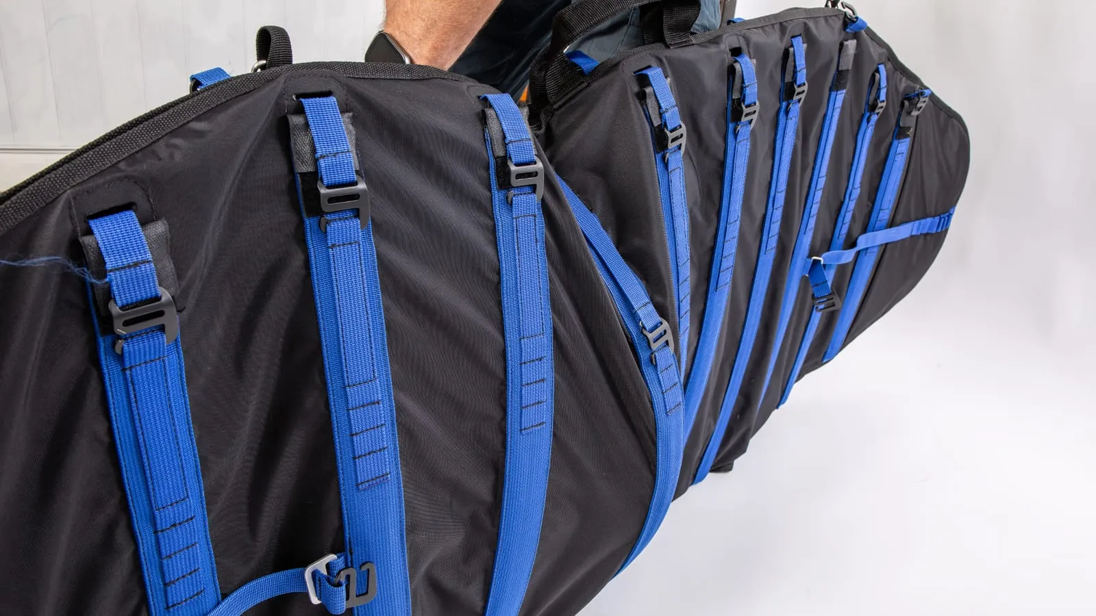 The loaded Ondo bag carried on a shoulder, seen from behind, showing the row of blue tensioned straps and buckles running the length of the padded body.