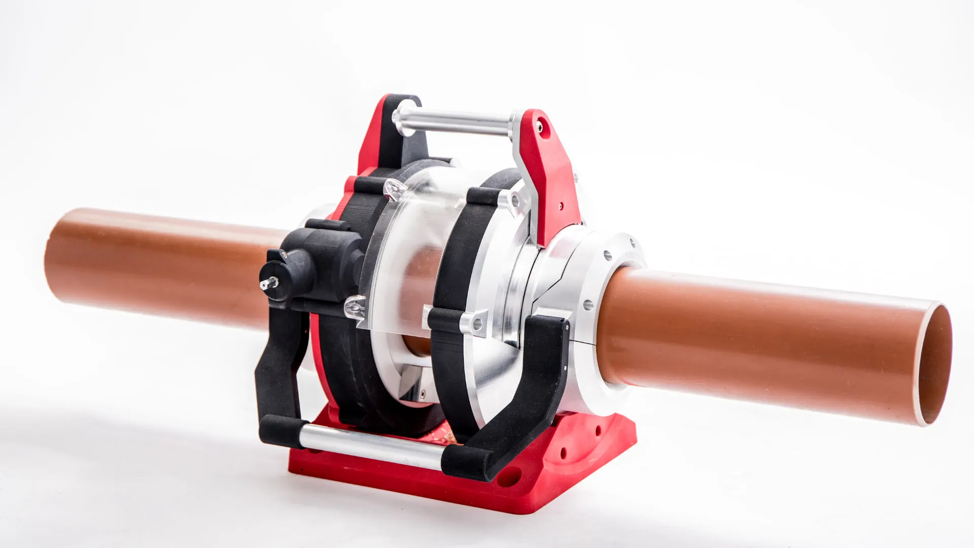 The tool clamped around a brown 110mm underground drainage pipe, with the pipe passing right through the rotating head and the tool sitting on its red base.