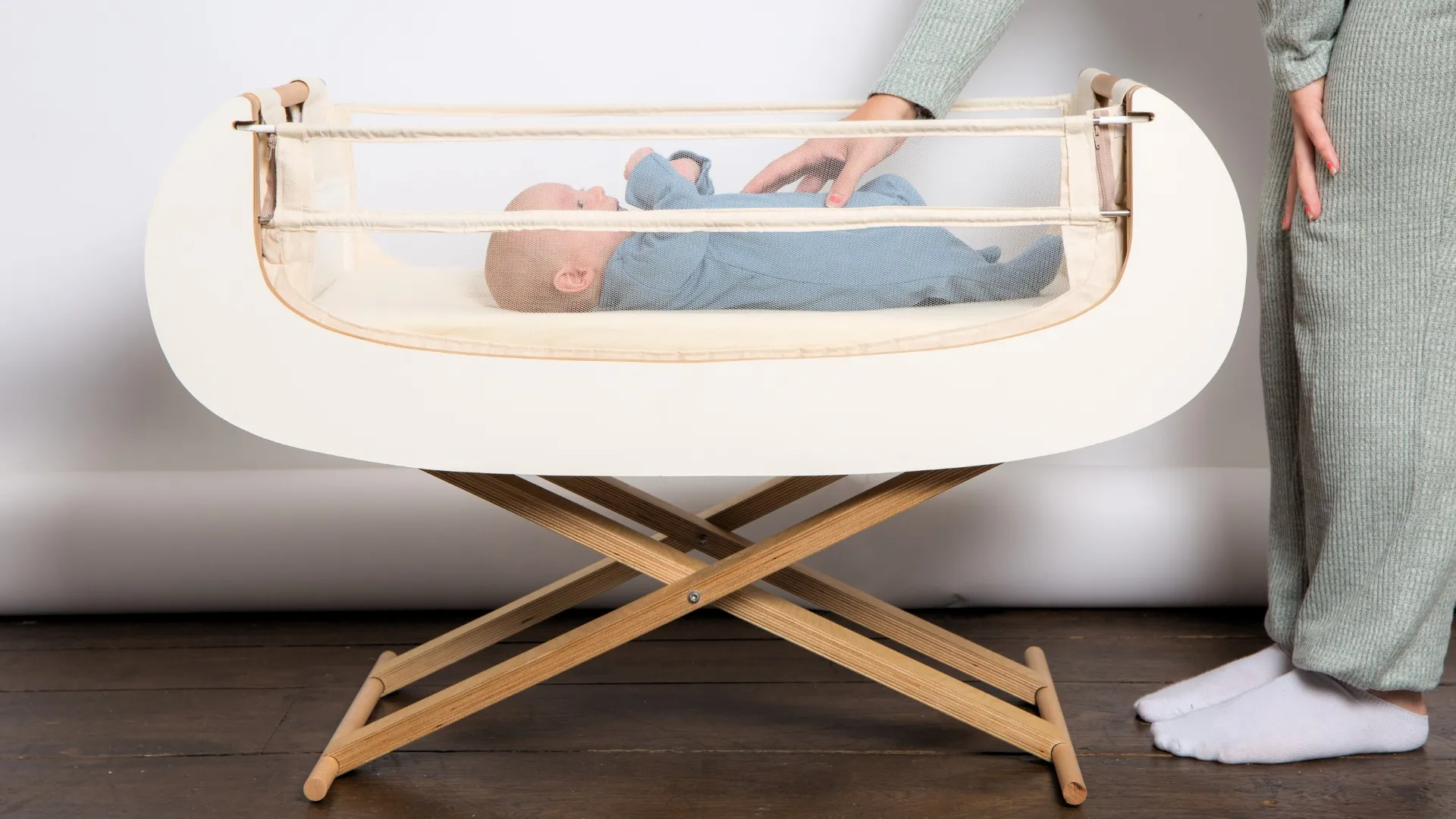 A baby lying in the Alora crib on its folding wooden stand